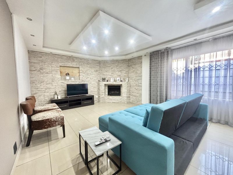 Spacious living room featuring a modern stone-clad feature wall, built-in fireplace, recessed ceiling with downlights, and large tiled flooring.