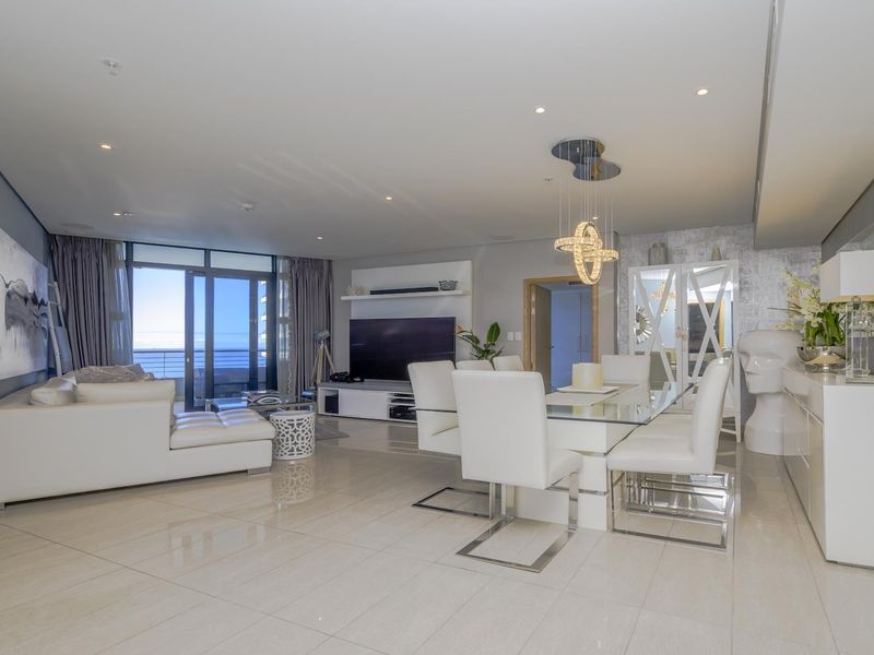 Spacious open-plan living and dining area featuring polished porcelain tiles, recessed lighting, and seamless access to a private balcony with ocean views.