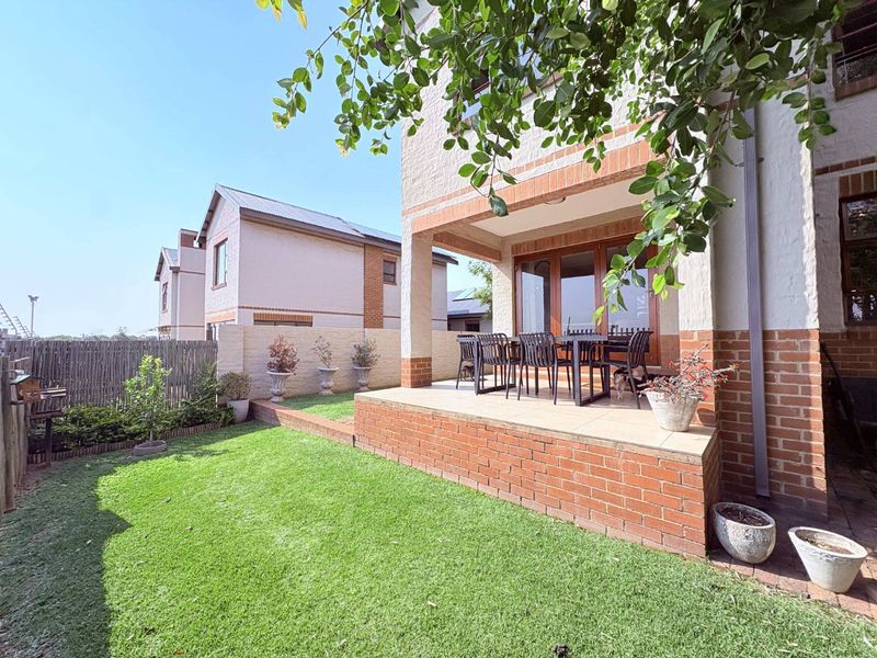 A rear view of the townhouse featuring a covered patio with tiled flooring, brick accents, and a well-maintained private garden area.