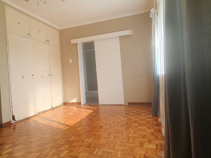 A spacious bedroom featuring classic parquet flooring, extensive built-in cupboards, and a sliding door leading to an en-suite bathroom.