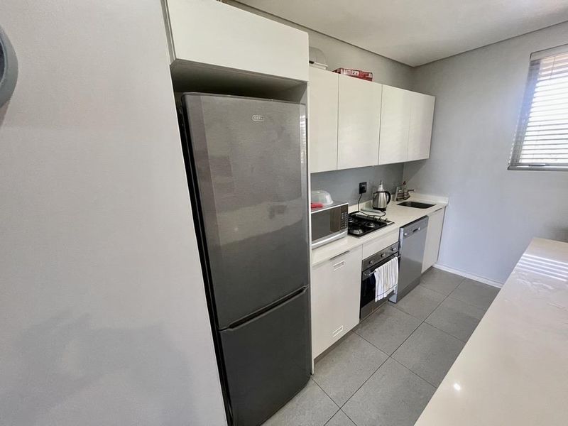 A functional kitchen featuring white cabinetry, stainless steel appliances including an oven and hob, tiled flooring, and a window with venetian blinds.