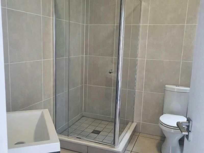 A clean, modern bathroom featuring a glass shower enclosure, a white toilet, and a vanity cabinet with a basin, finished with neutral wall and floor tiles.
