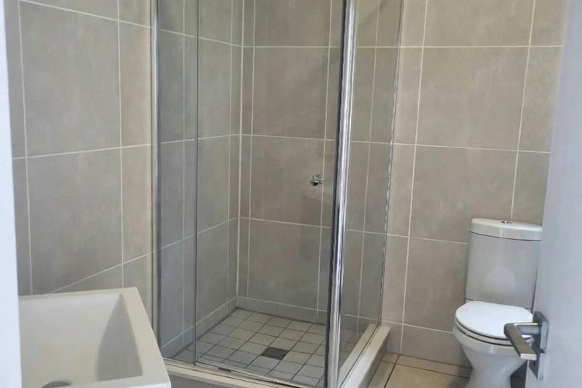 A clean, modern bathroom featuring a glass shower enclosure, a white toilet, and a vanity cabinet with a basin, finished with neutral wall and floor tiles.