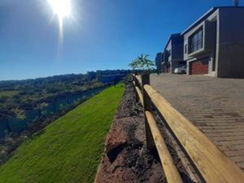 Exterior view of the townhouse complex featuring a paved driveway, timber fencing, and a landscaped embankment overlooking the surrounding area.