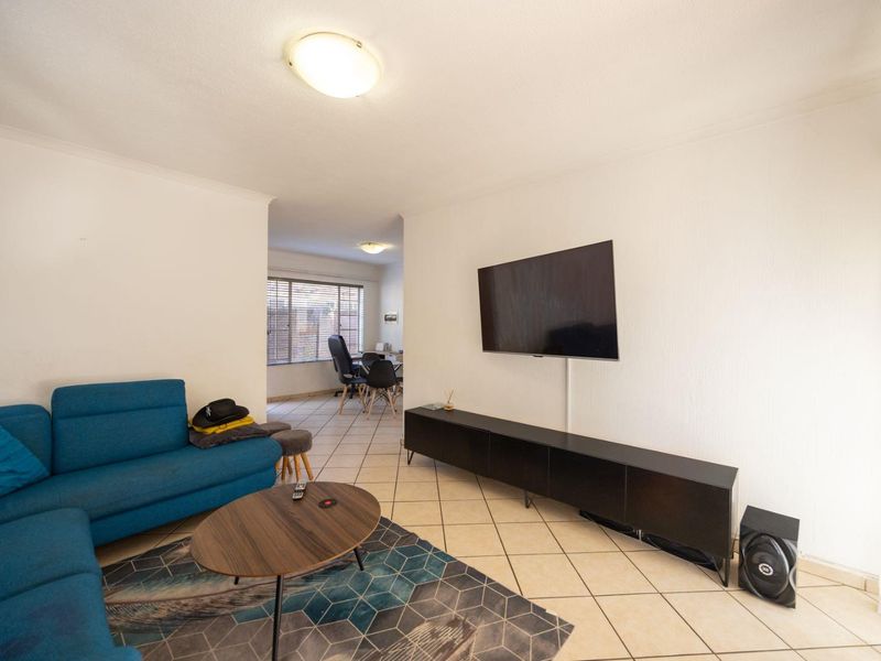 A living room featuring tiled flooring and a wall-mounted television setup, with an open-plan layout leading to an adjacent dining area.