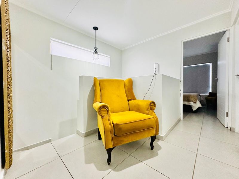 A bright, tiled hallway area featuring a half-height partition wall, modern pendant lighting, and a horizontal window, leading into an adjacent bedroom.