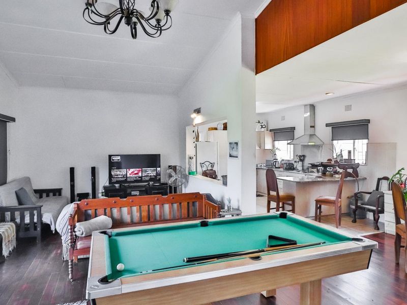 Spacious open-plan living and dining area featuring timber flooring, a central kitchen island, and a convenient pass-through window connecting to the kitchen.