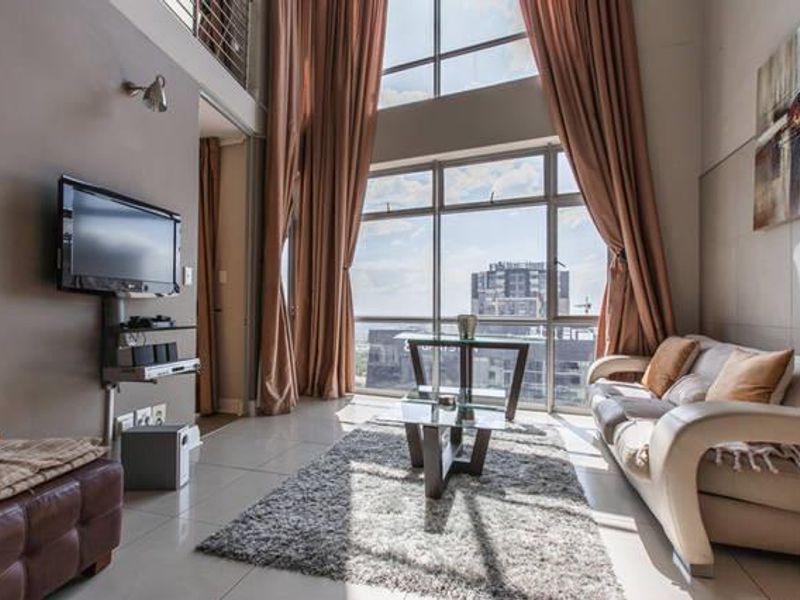 Spacious double-volume living room featuring floor-to-ceiling windows with city views, tiled flooring, and a mezzanine level overlooking the main area.