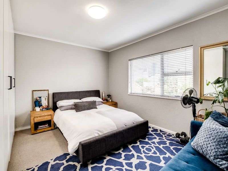 A well-maintained bedroom featuring neutral walls, carpeted flooring, a large built-in wardrobe, and a window fitted with venetian blinds.
