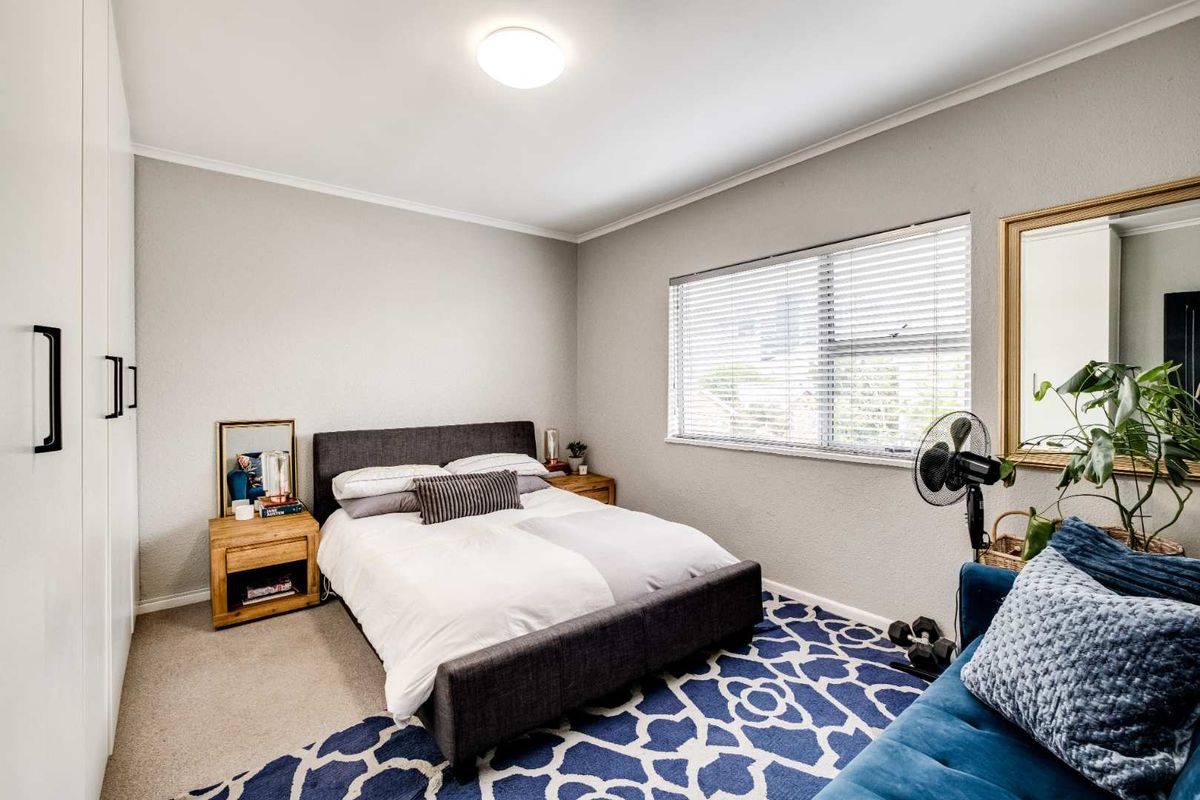 A well-maintained bedroom featuring neutral walls, carpeted flooring, a large built-in wardrobe, and a window fitted with venetian blinds.