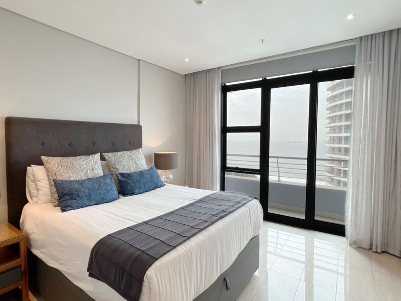 Modern bedroom featuring large floor-to-ceiling windows with balcony access, sleek tiled flooring, and built-in wardrobe storage.