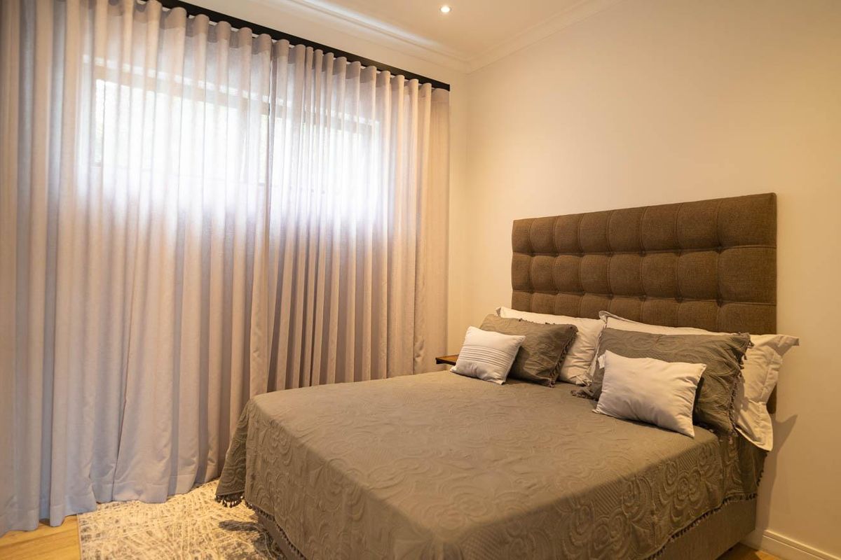 A well-maintained bedroom featuring neutral tones, recessed ceiling lighting, and floor-to-ceiling curtains.
