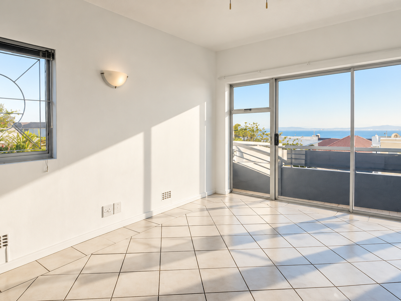 A bright, empty living area featuring tiled floors, large sliding glass doors leading to a balcony, and expansive views of the ocean.