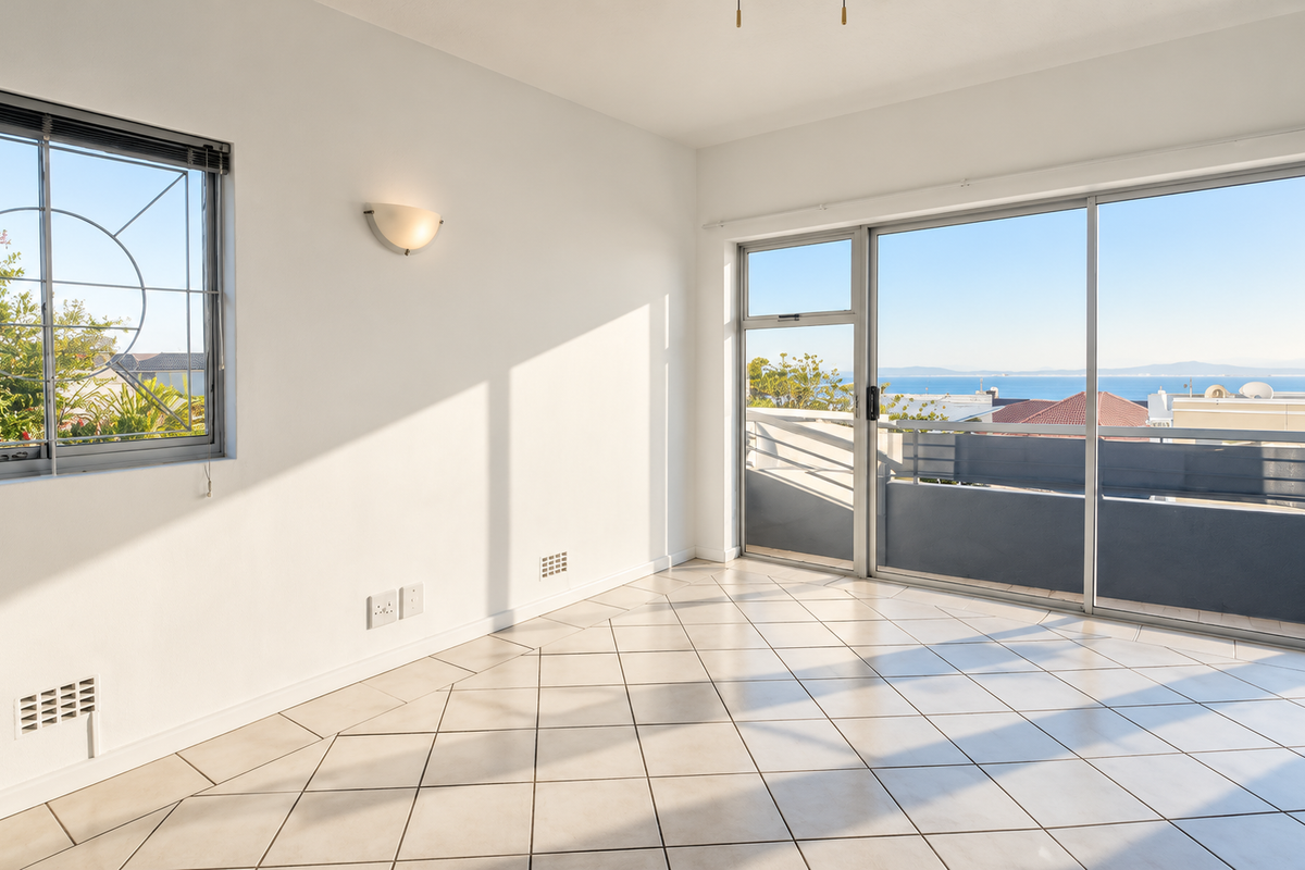 A bright, empty living area featuring tiled floors, large sliding glass doors leading to a balcony, and expansive views of the ocean.