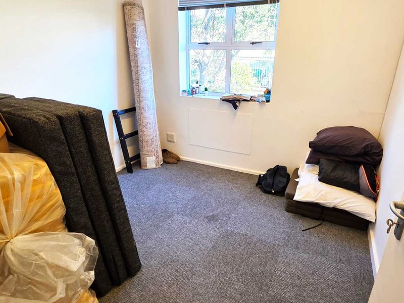 A small office space featuring carpeted flooring and a window, currently used for storage.