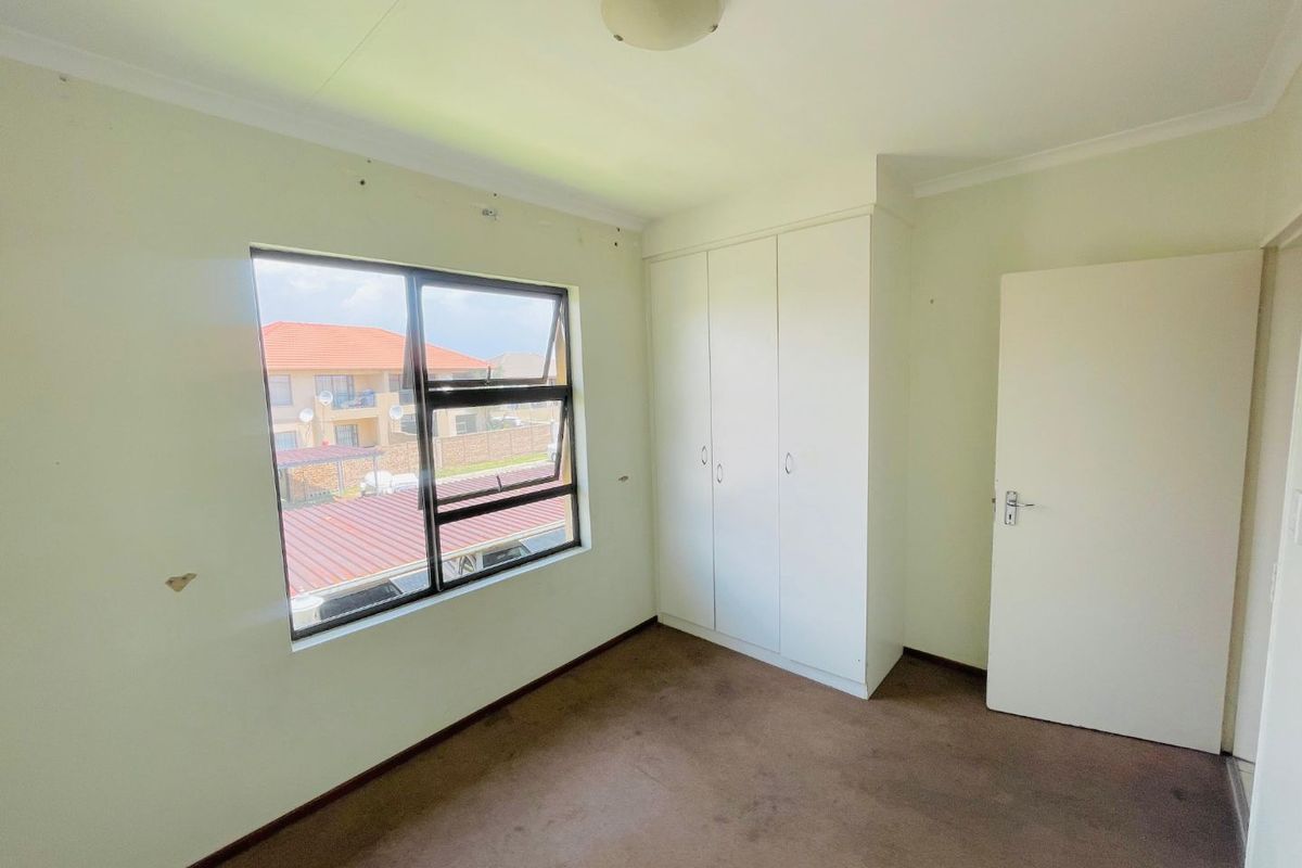 A bedroom featuring built-in cupboards, carpeted flooring, and a window with views of the surrounding complex.