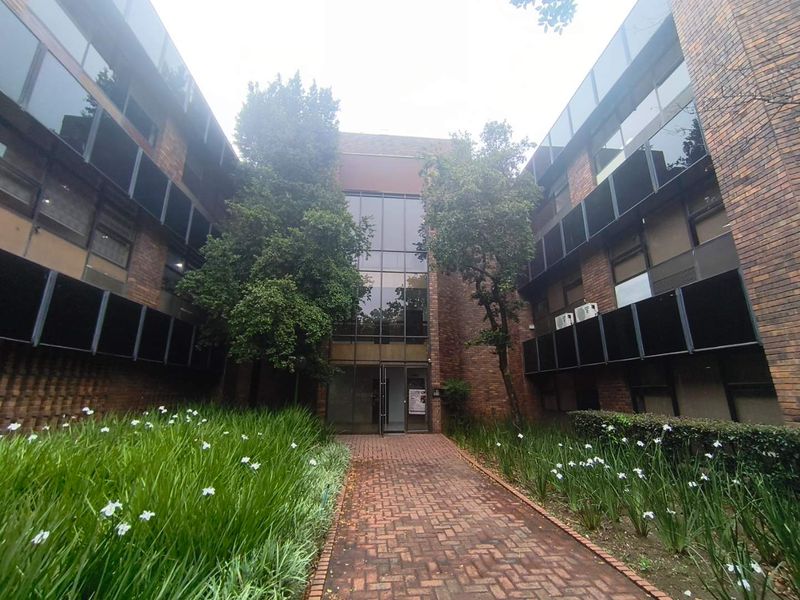 Front entrance view of a multi-story office building featuring a brick facade, glass curtain wall, and a paved walkway leading to the main entry.