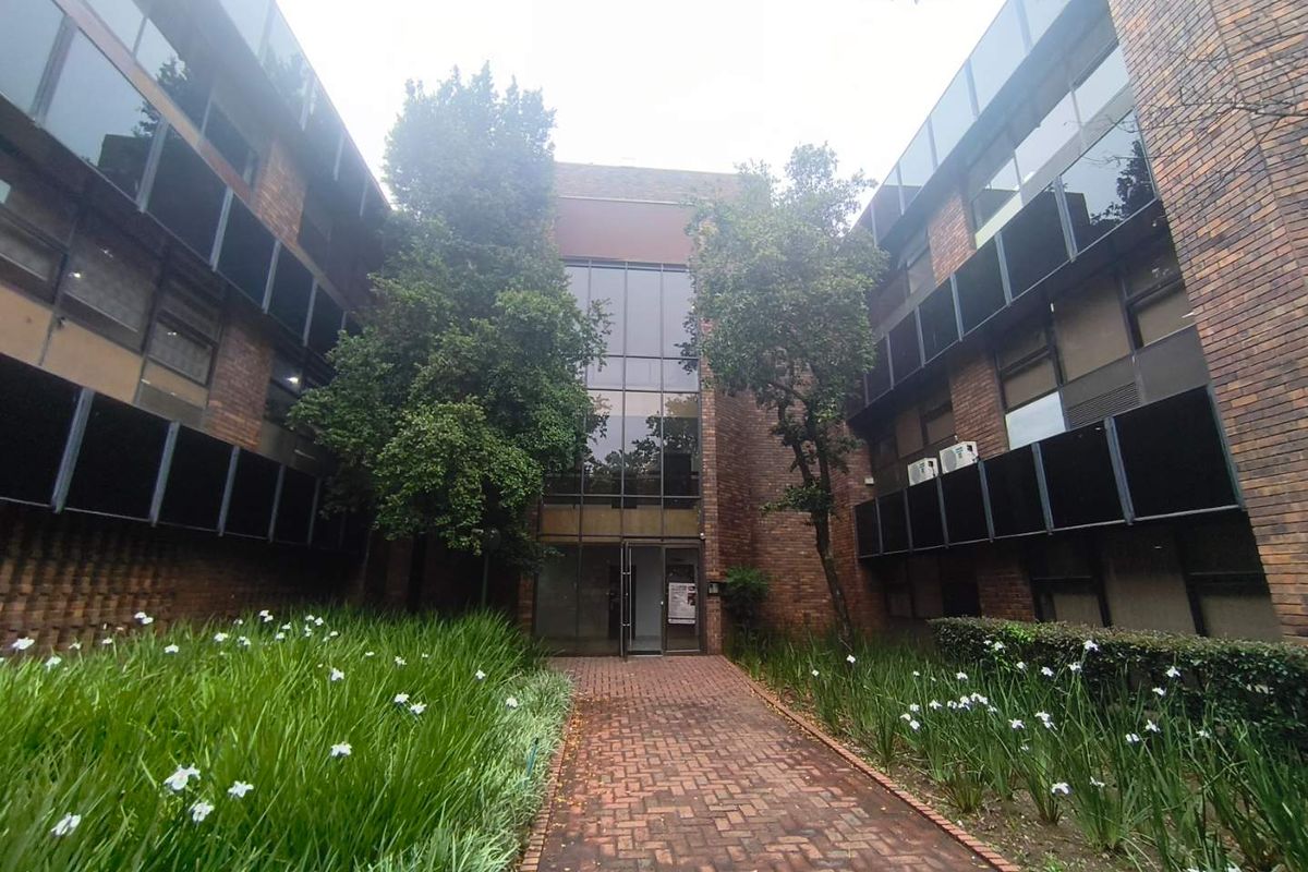Front entrance view of a multi-story office building featuring a brick facade, glass curtain wall, and a paved walkway leading to the main entry.