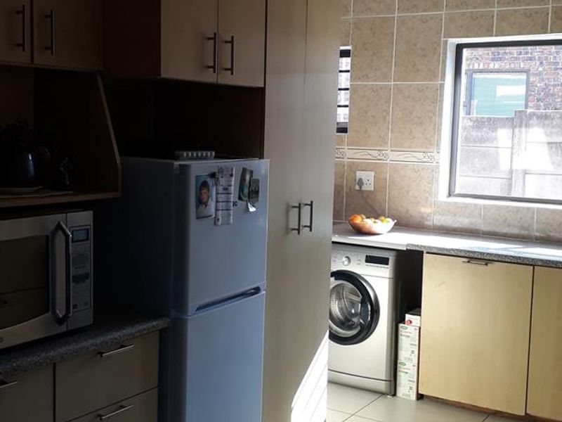 A functional kitchen featuring light-toned cabinetry, tiled walls, and tiled flooring, with dedicated space for laundry appliances and ample storage.