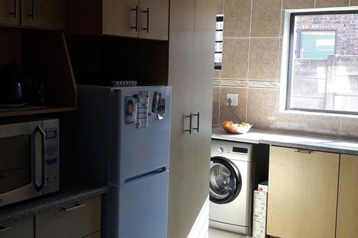 A functional kitchen featuring light-toned cabinetry, tiled walls, and tiled flooring, with dedicated space for laundry appliances and ample storage.