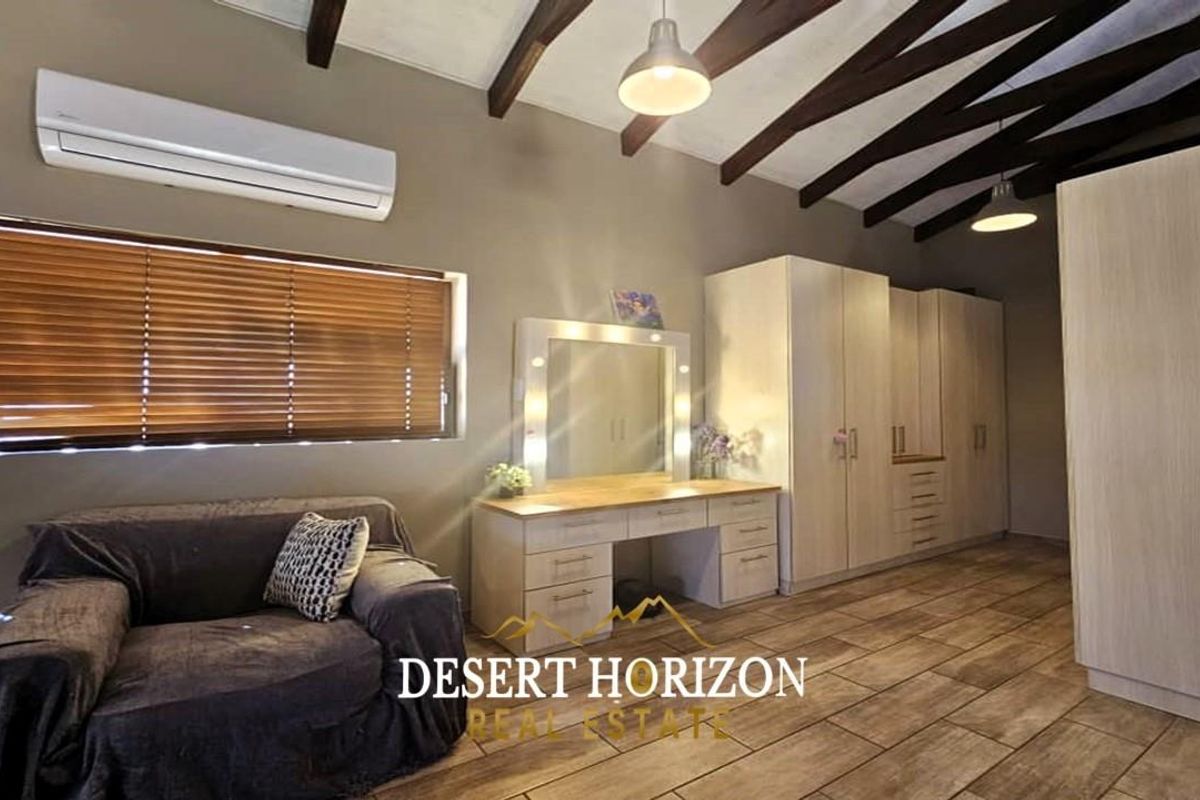 Spacious bedroom featuring exposed timber ceiling beams, built-in cabinetry, a vanity unit, and a wall-mounted air conditioning unit.