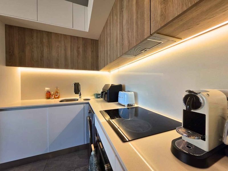 Modern kitchen featuring sleek wood-grain cabinetry, stone countertops, integrated induction cooktop, and ambient under-cabinet LED lighting.