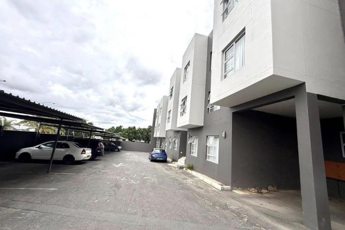 Exterior view of the apartment complex showing the rear parking area with covered bays and multi-story building facade.
