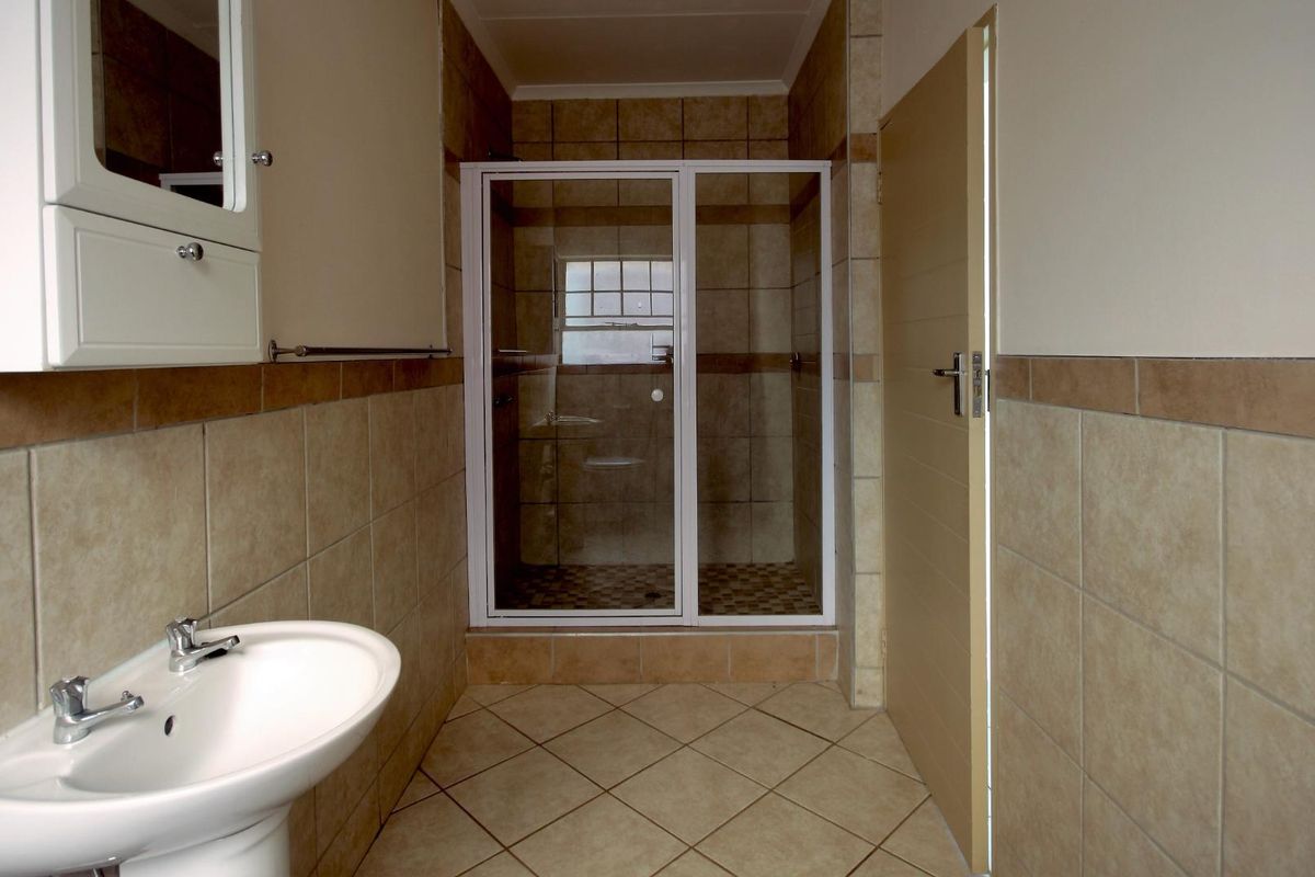 A functional bathroom featuring a pedestal basin, a tiled shower enclosure with a glass door, and neutral wall and floor tiling.