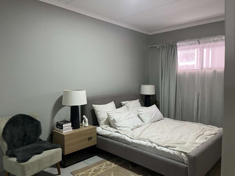 A well-maintained bedroom featuring neutral grey walls, coving, and a window with curtain fixtures.