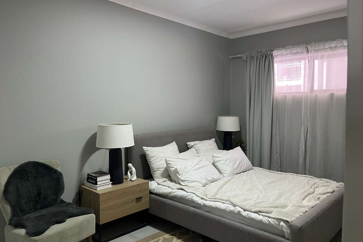 A well-maintained bedroom featuring neutral grey walls, coving, and a window with curtain fixtures.