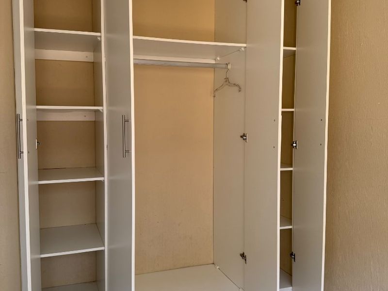 A bedroom featuring a large, white built-in wardrobe with ample shelving and hanging space, complemented by neutral tiled flooring.