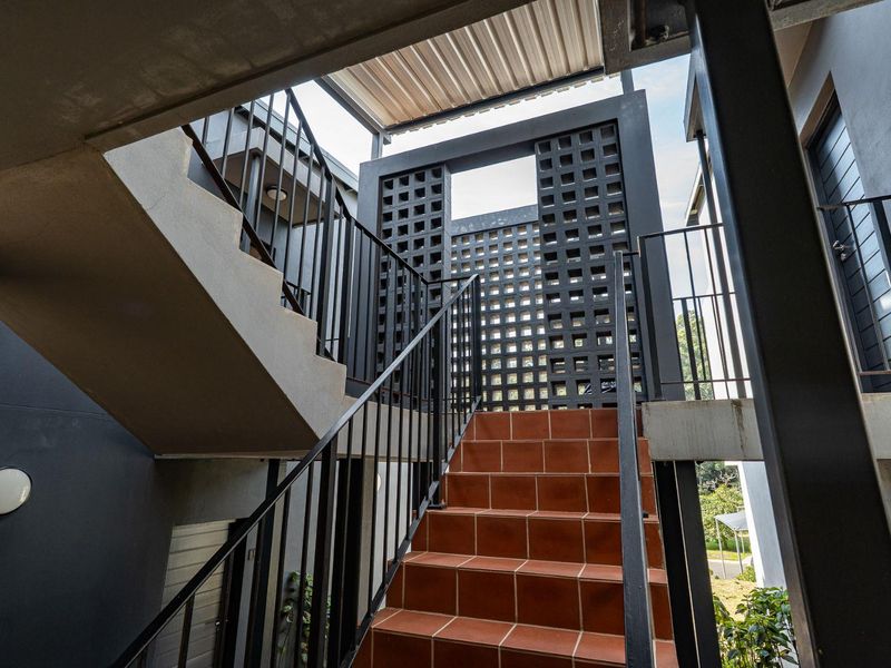 Modern outdoor staircase featuring tiled steps, metal railings, and a decorative breeze block screen providing architectural interest to the apartment entrance.