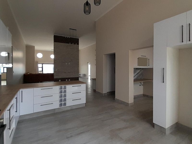 Spacious open-plan kitchen and living area featuring modern white cabinetry, wood-look countertops, and a dedicated scullery, finished with neutral tiling throughout.