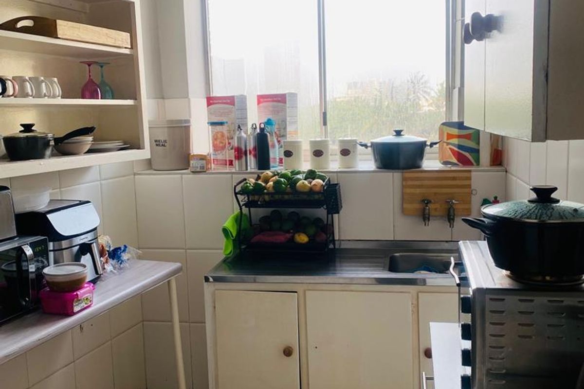 A compact kitchen featuring tiled splashbacks, built-in cabinetry, and a stainless steel sink, offering a functional layout with potential for modern updates.