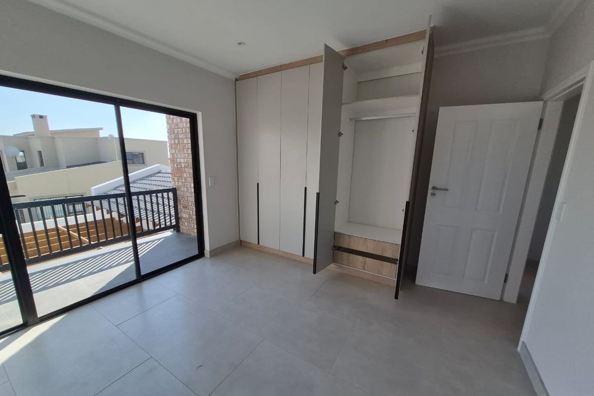 A bright, modern bedroom featuring neutral tiled flooring, built-in cupboards, and a sliding glass door leading to a private balcony.