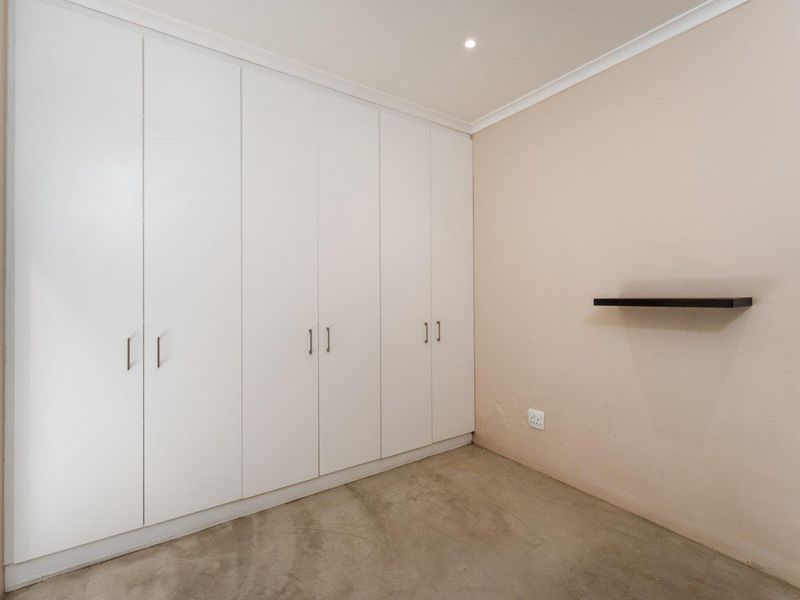 A clean, empty bedroom featuring extensive white built-in cupboards, recessed lighting, and a neutral wall finish, providing a versatile space ready for personalization.