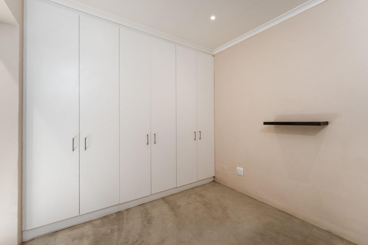 A clean, empty bedroom featuring extensive white built-in cupboards, recessed lighting, and a neutral wall finish, providing a versatile space ready for personalization.