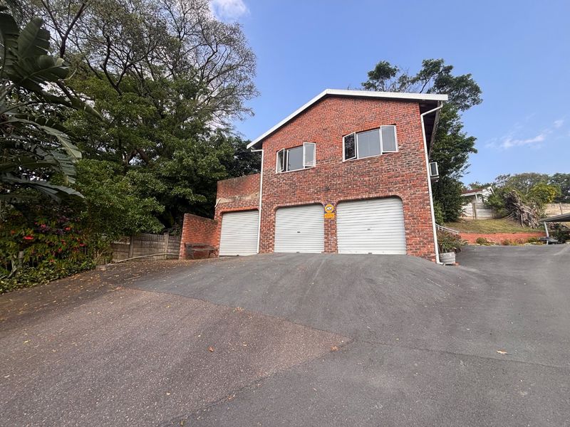 A double-story brick house featuring a triple garage with roller doors and an expansive asphalt driveway.