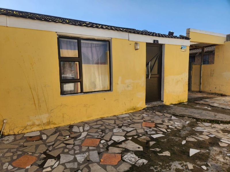 Front exterior view of a single-story house featuring a paved patio area, yellow painted walls, and a damaged entrance door.