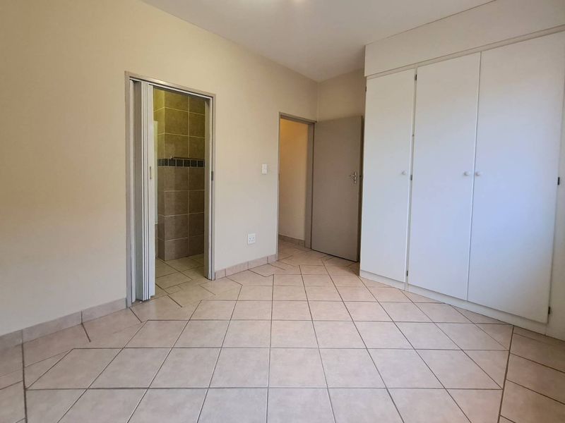 A clean, empty bedroom featuring neutral tiled flooring, built-in cupboards, and direct access to an en-suite bathroom.
