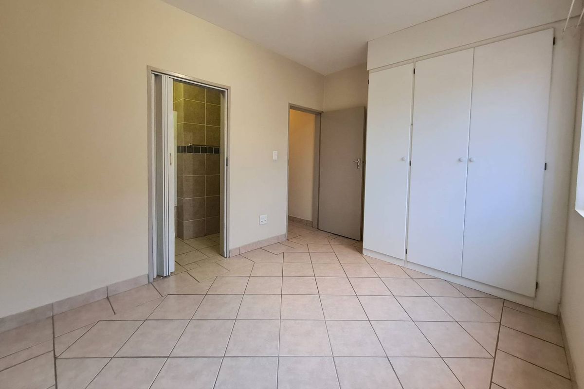 A clean, empty bedroom featuring neutral tiled flooring, built-in cupboards, and direct access to an en-suite bathroom.