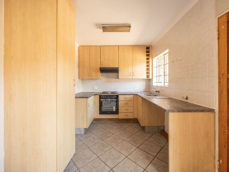 A functional kitchen featuring light wood cabinetry, laminate countertops, built-in oven with hob, and tiled flooring, offering a clean space ready for modern updates.