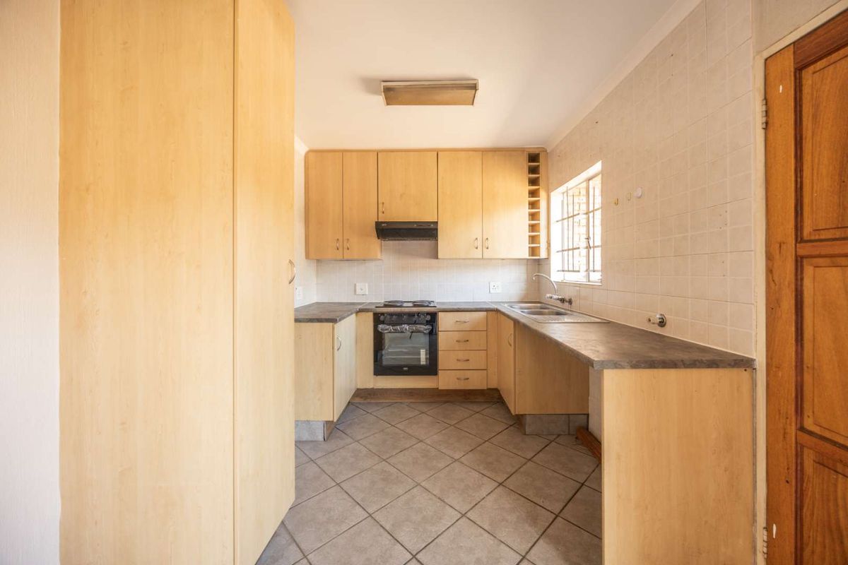 A functional kitchen featuring light wood cabinetry, laminate countertops, built-in oven with hob, and tiled flooring, offering a clean space ready for modern updates.