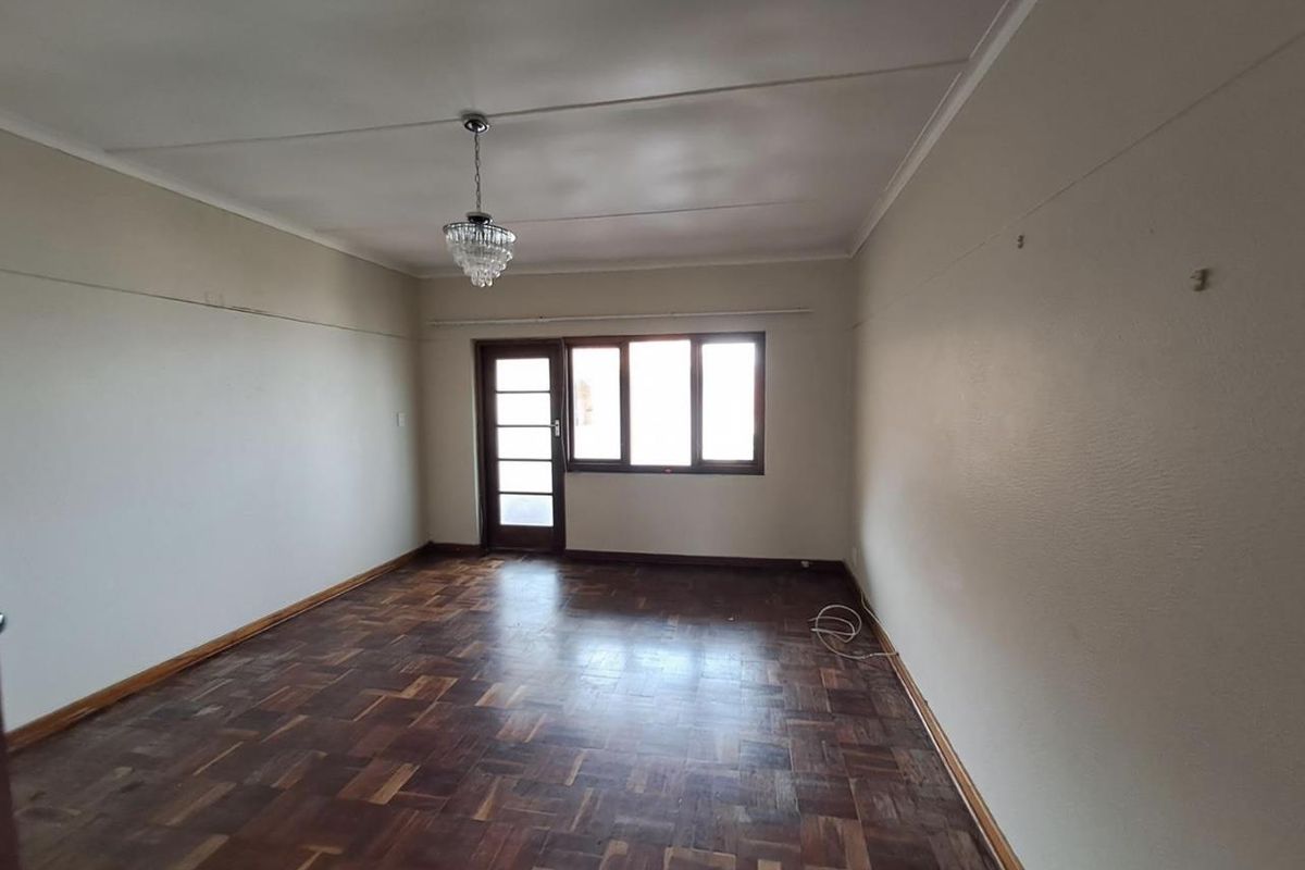 A spacious, empty living room featuring original parquet flooring, neutral walls, and a glass-paneled door leading to an outdoor area.