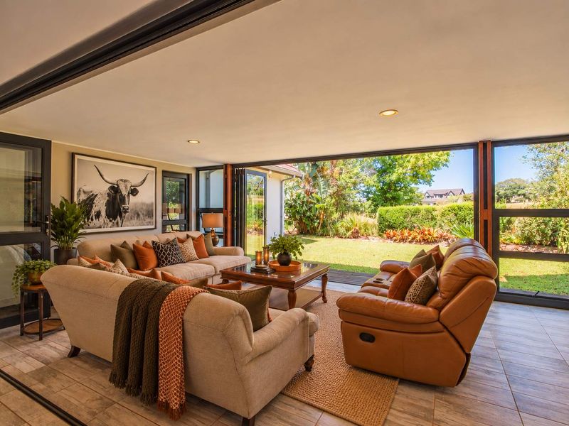 A bright and spacious living room featuring large stacking glass doors that open onto a landscaped garden, with modern tiled flooring and recessed lighting.
