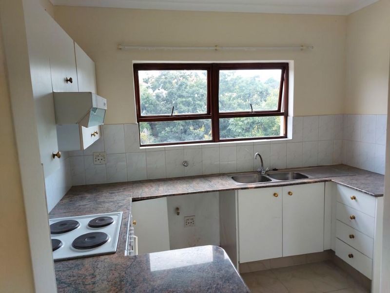 A functional kitchen featuring granite countertops, built-in cabinetry, an electric hob, and a double basin sink with a view through the window.