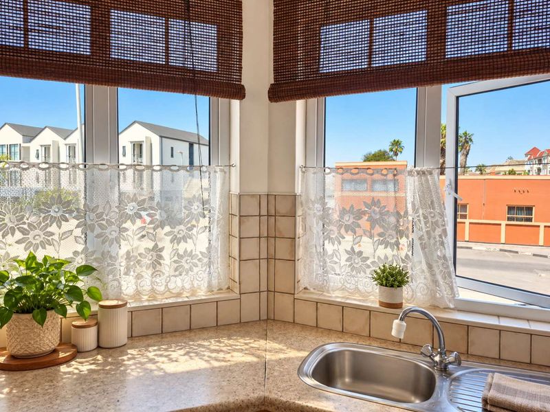A bright kitchen corner featuring a stainless steel sink, tiled splashback, and large windows with natural light.