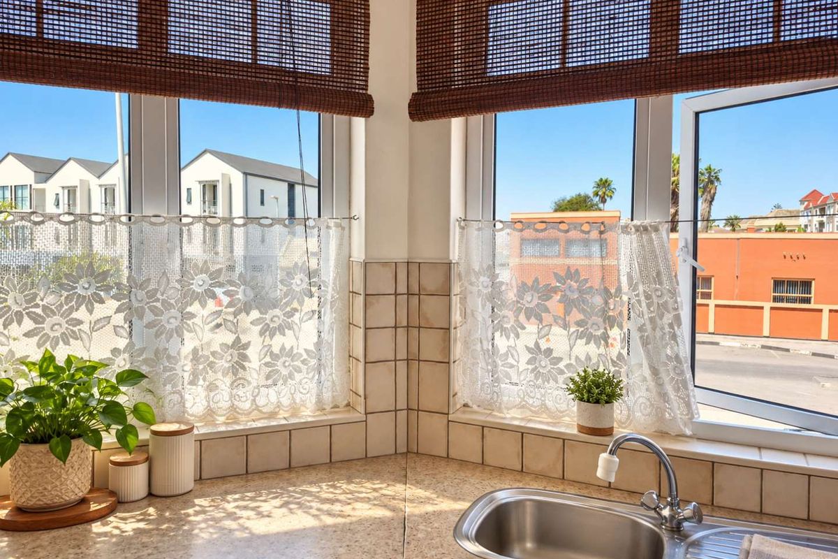 A bright kitchen corner featuring a stainless steel sink, tiled splashback, and large windows with natural light.