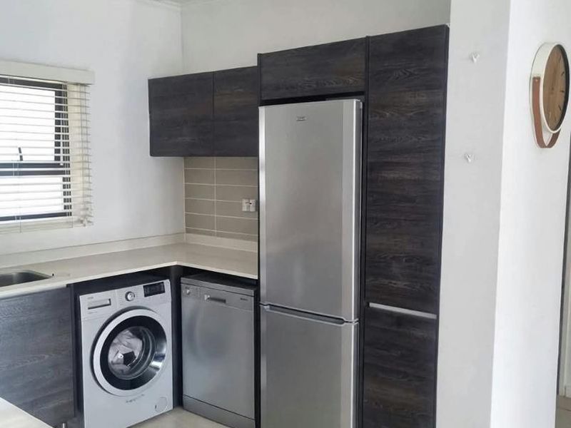 A functional kitchen featuring dark wood-grain cabinetry, light countertops, tiled backsplash, and integrated appliance spaces with tiled flooring.