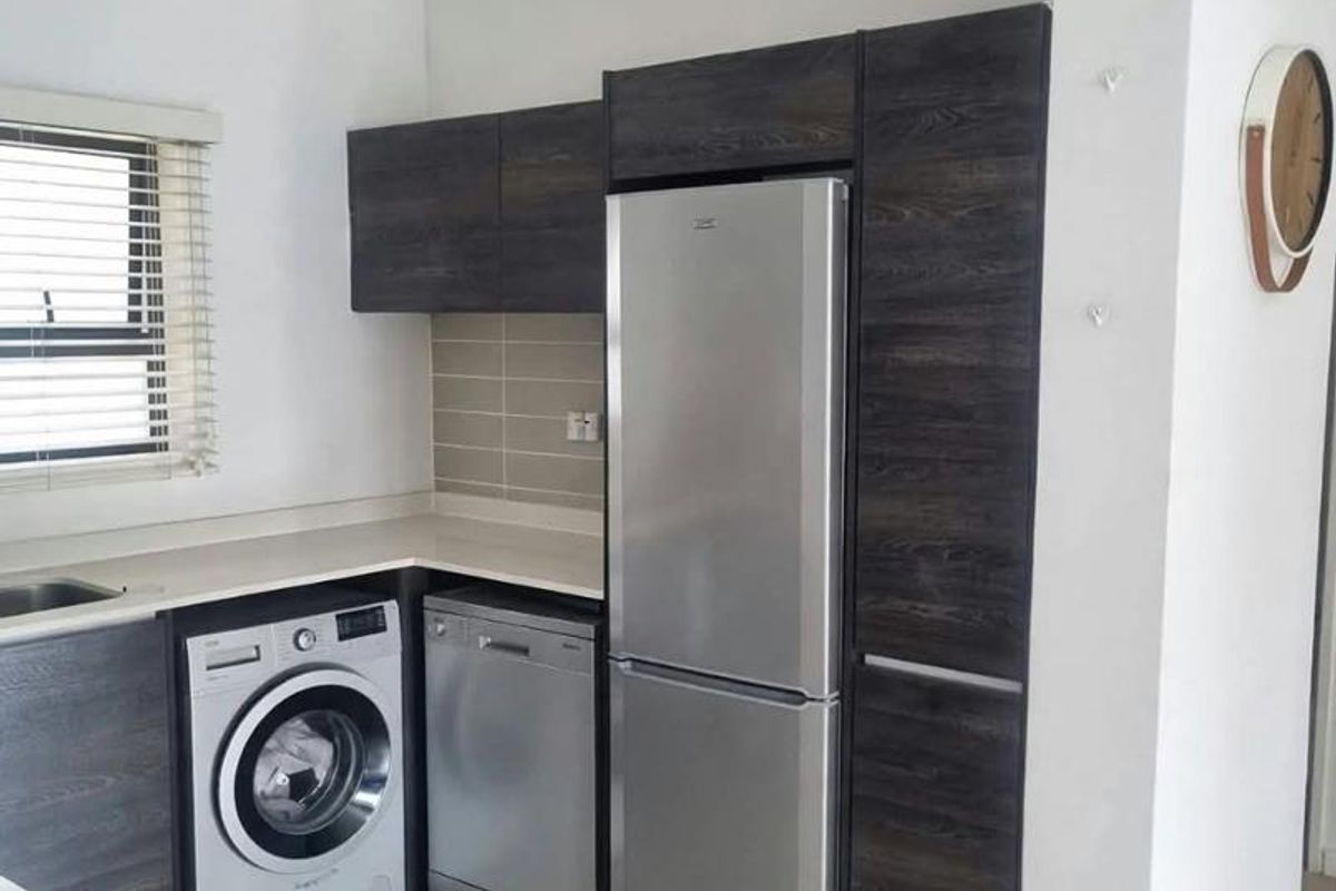 A functional kitchen featuring dark wood-grain cabinetry, light countertops, tiled backsplash, and integrated appliance spaces with tiled flooring.